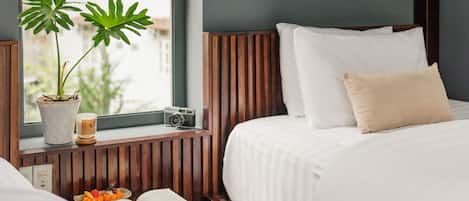 A hotel room with a bed, a bedside table with a book and decorative items, a potted plant, and a window with a view.