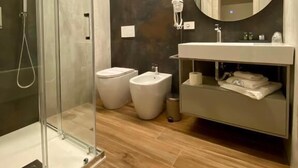 Un baño moderno con cabina de ducha de vidrio, un espejo redondo, tocador con lavabo y dos bidés.