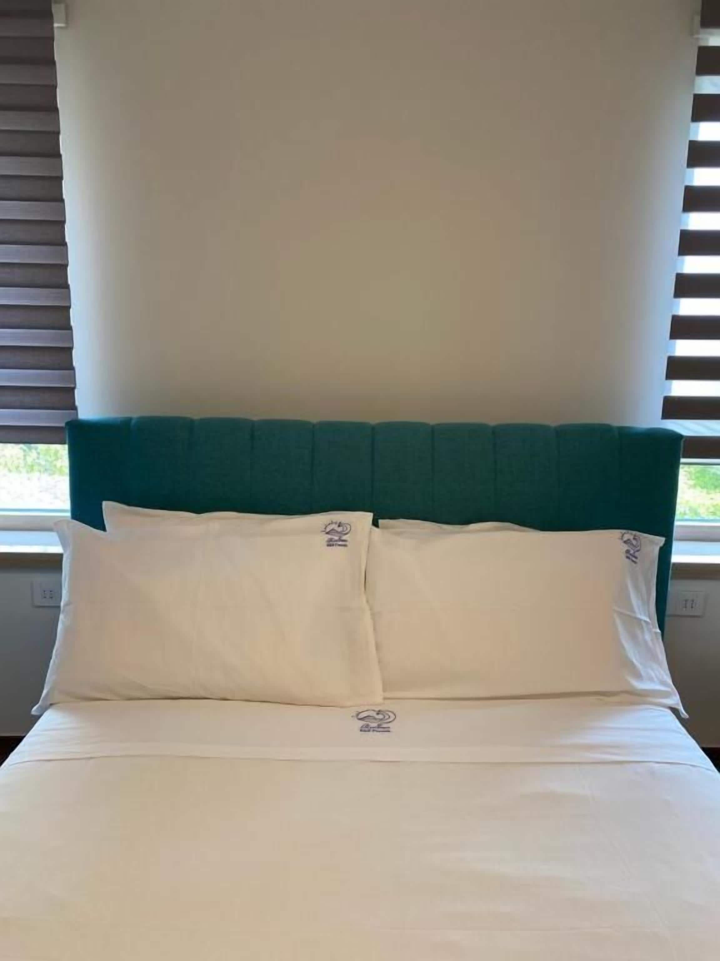 A bed with white bedding and a teal headboard, positioned against a wall with a window.