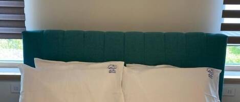 A bed with white bedding and a teal headboard, positioned against a wall with a window.