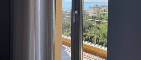 Ein Zimmer mit einer Schiebetür, die auf einen Balkon mit Blick auf eine Stadtlandschaft und Grünflächen führt.