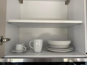 A stainless steel kitchen cabinet with white shelves, a white mug, and stacked white plates.