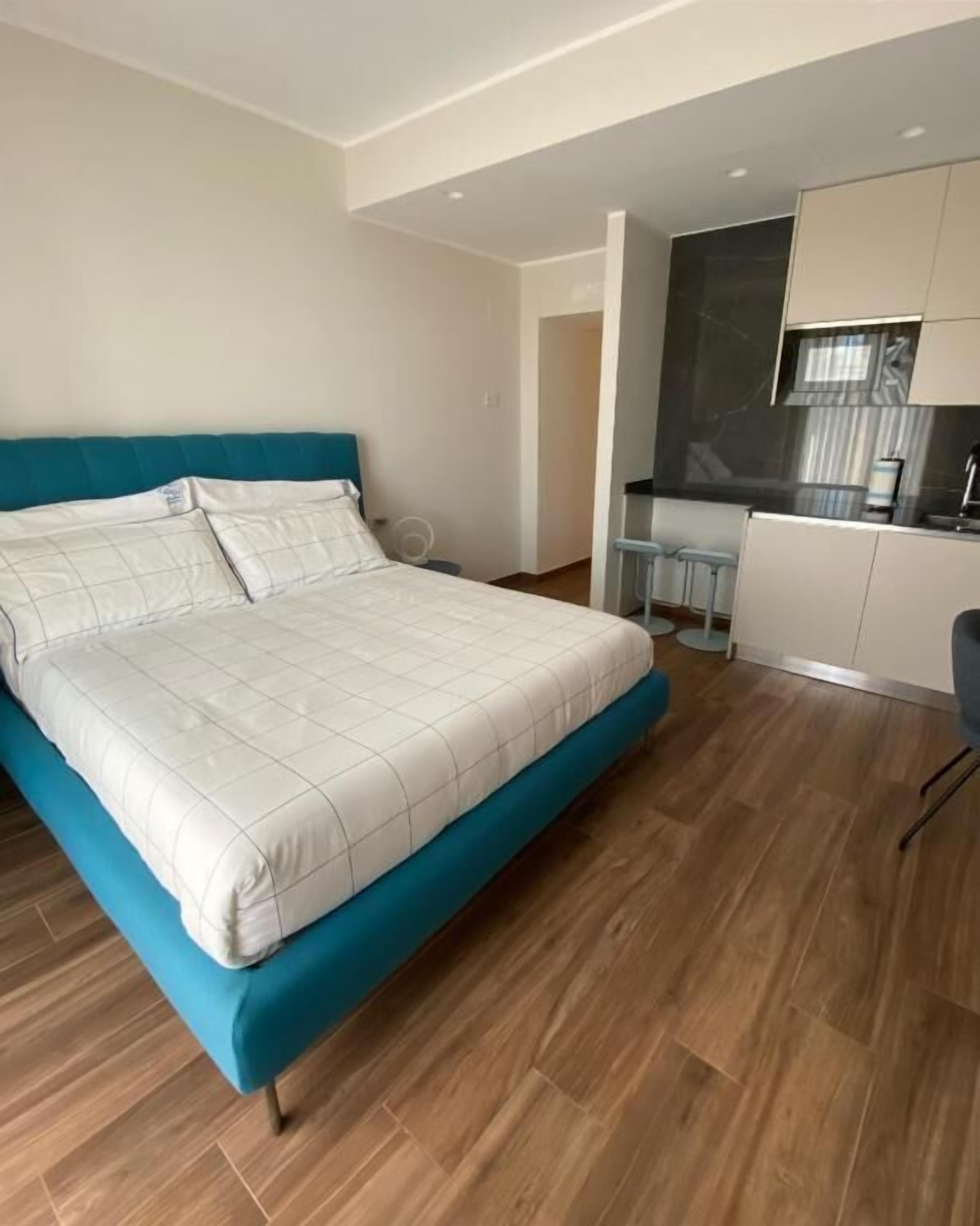 Un dormitorio moderno con una cama grande, una kitchenette y un baño visible a través de una puerta abierta.