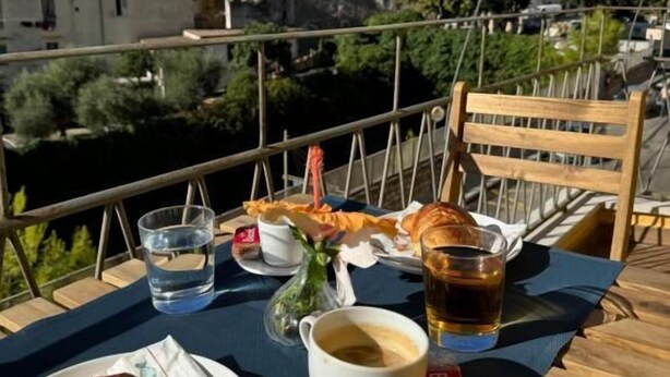 A table with a croissant, coffee cup, and glass of water, overlooking a cityscape with buildings and a tower. - RoSea B&B (Formia)