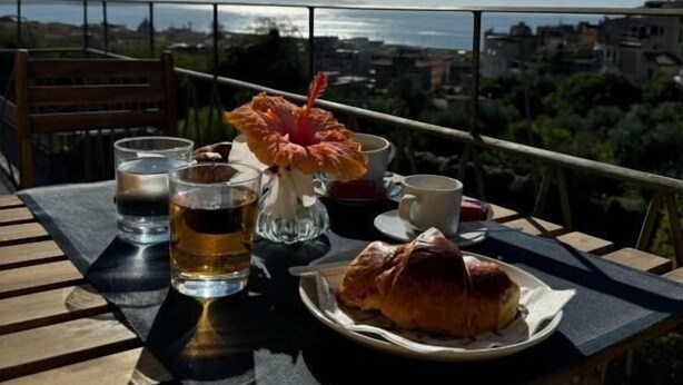 Una mesa con un plato de comida, un vaso de bebida y una flor en un balcón con vistas a la ciudad.