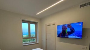 Un dormitorio con una cama, televisión montada en la pared, una ventana y una puerta.