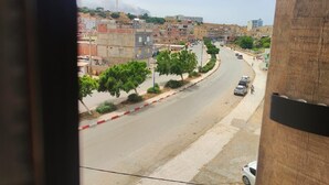 Vista da rua com edifícios, árvores e carros estacionados.