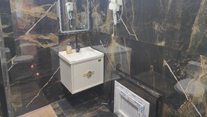 Casa de banho com parede de mármore, lavatório branco com torneira dourada e espelho em cima.