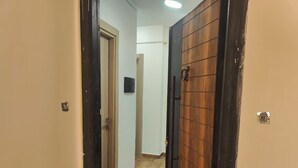 Um corredor com porta de madeira, parede branca e chão de azulejos.