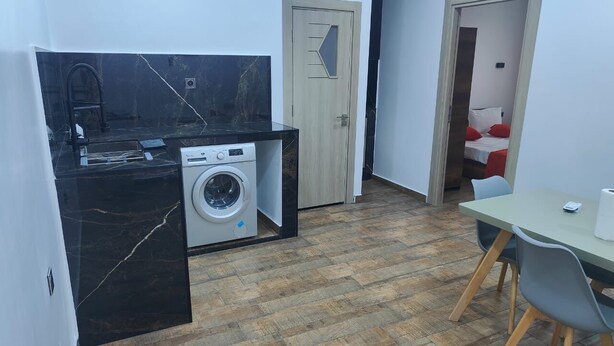 Uma cozinha compacta com máquina de lavar, porta de madeira e área de refeições com mesa e cadeiras.