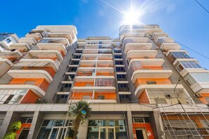 Un edificio residencial de varios pisos con balcones, amplias ventanas y una palmera frente a él.
