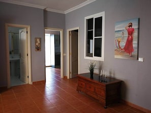 Een gang met een houten kast, een schilderij en een deur naar een andere kamer.