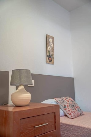 A bedroom with a wooden nightstand, a lamp, a bed with a patterned pillow, and a wall-mounted painting. - Sol y Luna · house with terrace and barbecue in Caleta de Fuste (Castillo Caleta de Fuste)