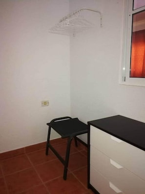Ein kleines Zimmer mit Schreibtisch, Stuhl und einer Kleiderstange.