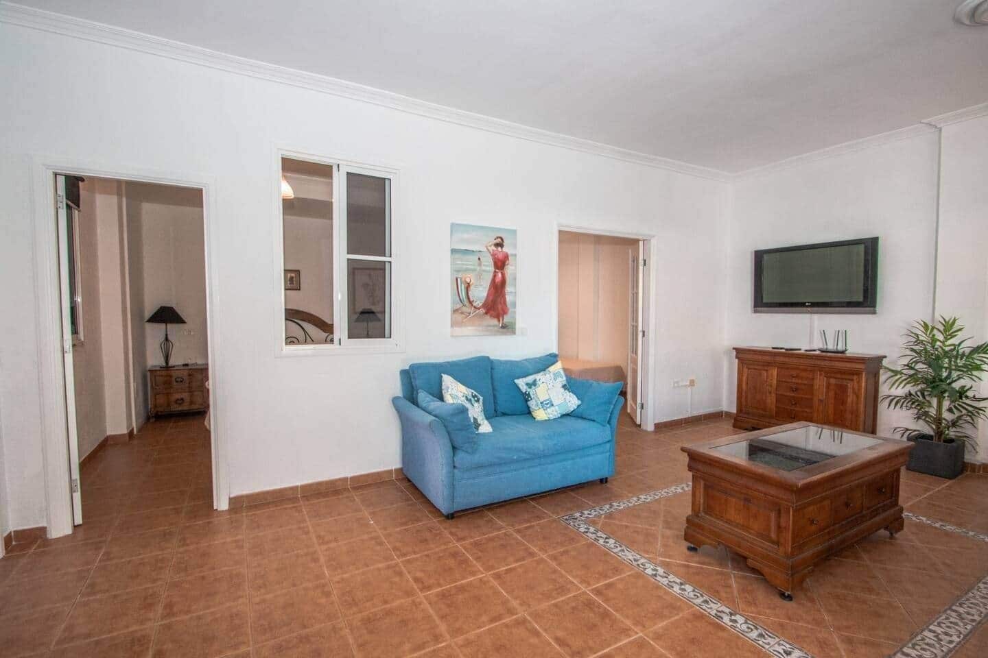 A living room with a blue sofa, a wooden cabinet, a TV, and a potted plant.