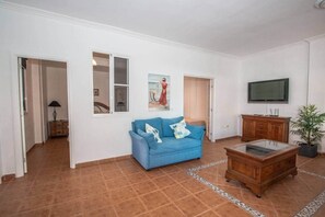 Ein Wohnzimmer mit einem blauen Sofa, einem Holzschrank, einem Fernseher und einer Topfpflanze.