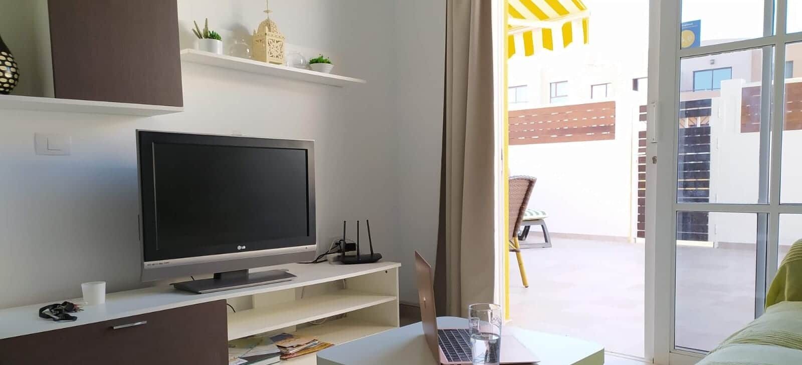 Ett modernt rum med en platt-TV, en bärbar dator och en matplats med en stol och ett bord.