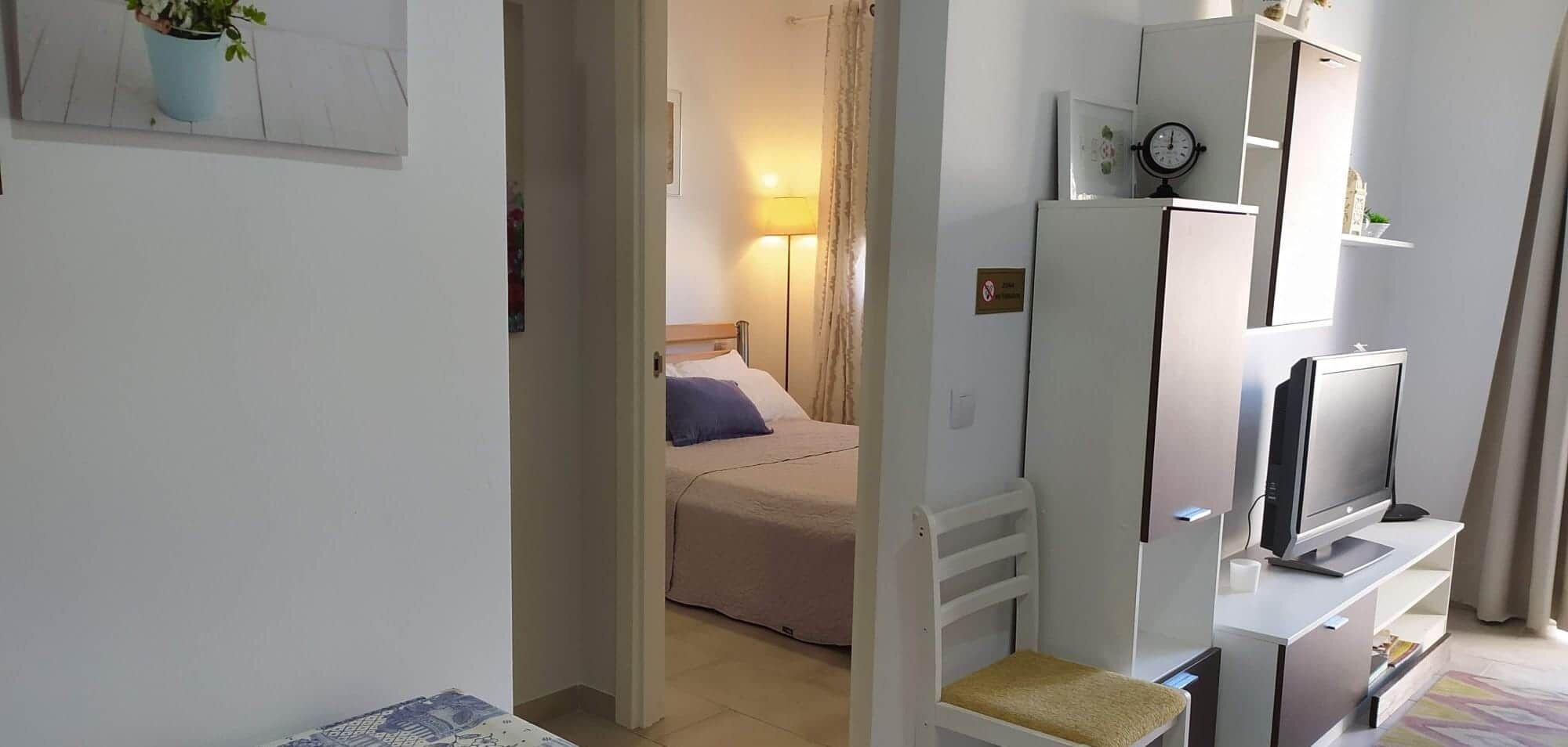 Una habitación de hotel con cama, televisión, lámpara y reloj en la pared.