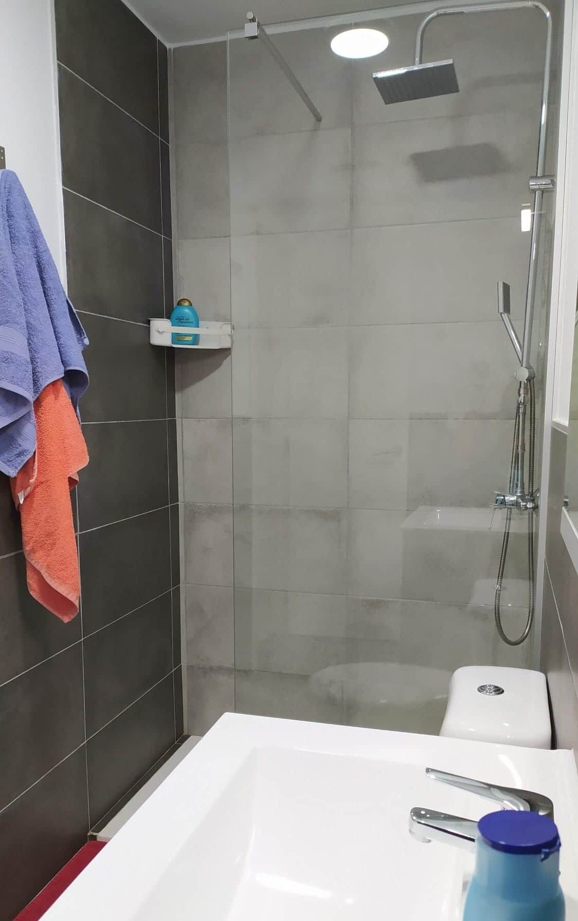 A modern bathroom with a shower, a white sink, and a toilet.