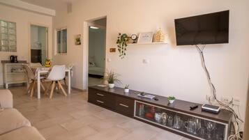Una sala de estar moderna con un televisor de pantalla plana, un comedor con mesa y sillas, y una cocina con hervidor.