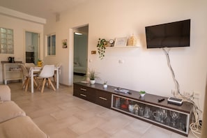 Una sala de estar moderna con un televisor de pantalla plana, un comedor con mesa y sillas, y una cocina con hervidor.