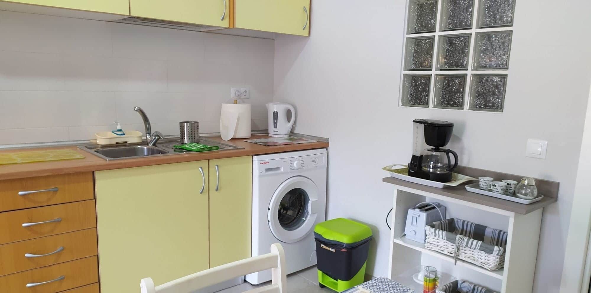 A compact kitchen with a washing machine, a coffee maker, and a small dining area.