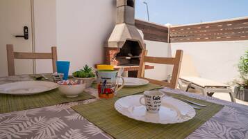 Un espacio para comer al aire libre con un horno de ladrillo, individuales verdes y una mesa preparada para dos.