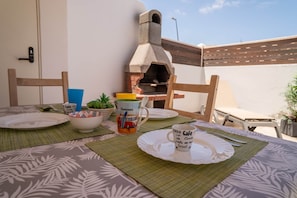 Un espacio para comer al aire libre con un horno de ladrillo, individuales verdes y una mesa preparada para dos.