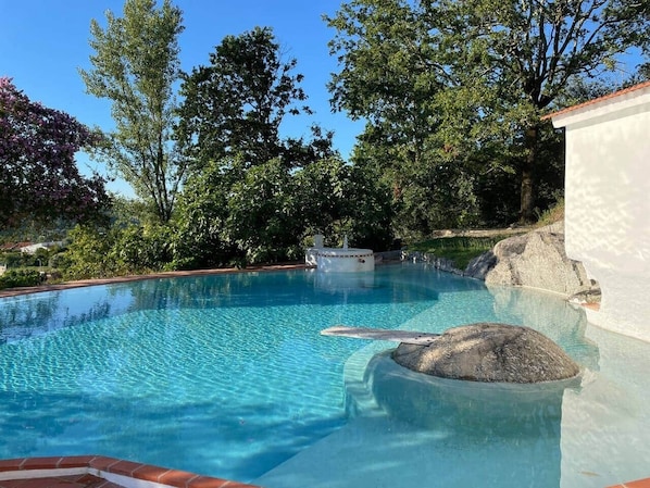 A clear swimming pool with a rock feature, surrounded by trees and a white building. - Private suite with views · Quinta da Agrela (Portugal) (Vade (São Pedro))