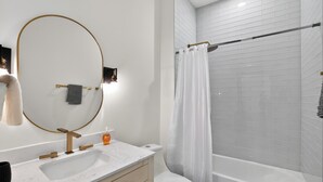 A modern bathroom with a white sink, gold faucets, a large mirror, a toilet, and a shower with a glass door. - Spacious 2-bedroom with modern finishes (Austin)
