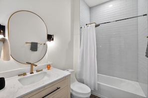 Ein modernes Badezimmer mit einem weißen Waschbecken, goldenen Armaturen, einem großen Spiegel, einer Toilette und einer Dusche mit Glastür.