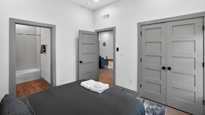 A bedroom with a bed, grey wardrobe, and a bathroom with a shower and bathtub. - Spacious 2-bedroom with modern finishes (Austin)