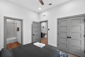 A bedroom with a bed, grey wardrobe, and a bathroom with a shower and bathtub. - Spacious 2-bedroom with modern finishes (Austin)