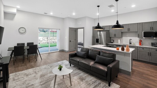 A modern kitchen with grey cabinets, a central island, and a dining area with a sofa and chairs. - Spacious 2-bedroom with modern finishes (Austin)