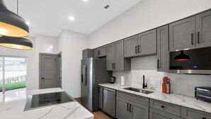 A modern kitchen with grey cabinets, a stainless steel refrigerator, a built-in oven, and a black pendant light. - Spacious 2-bedroom with modern finishes (Austin)