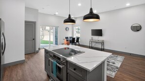 A modern kitchen with a central island, stainless steel appliances, pendant lighting, and a dining area with a TV and seating. - Modern 2-bedroom featuring spacious open-concept (Austin)