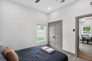 Ein Schlafzimmer mit Bett, Fenster, Tür und Blick ins Freie.