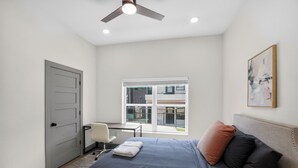 A bedroom with a bed, a desk, a chair, a ceiling fan, a window, and a door. - Modern 2-bedroom featuring spacious open-concept (Austin)
