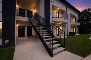 A multi-story building with a central staircase, balconies, and a well-lit entrance. - Elegant 2-bedroom with upscale finishes throughout. (Austin)