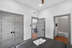 A hotel room with a bed, grey doors, a bathroom with a bathtub, and a hallway leading to another room. - Elegant 2-bedroom with upscale finishes throughout. (Austin)