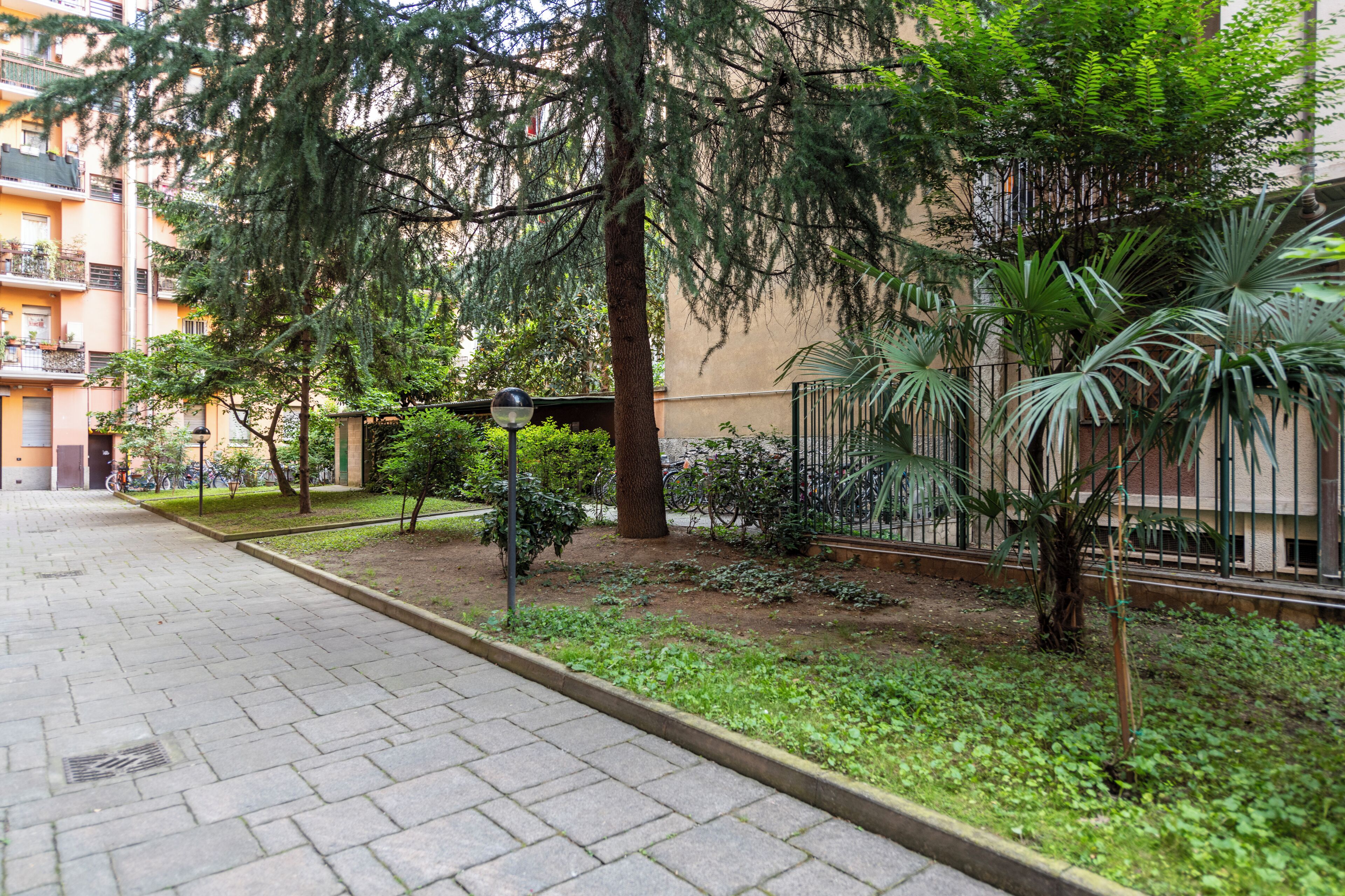 A paved walkway, trees, and a building with balconies.