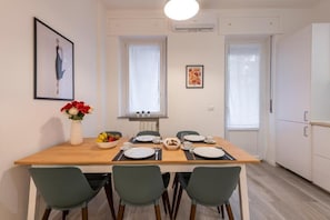 Een eetgedeelte met een houten tafel voor vier personen, twee stoelen, een bloevas en een schaal fruit.