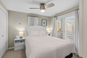 Une chambre à coucher avec un lit, des tables de chevet, un ventilateur de plafond et une fenêtre avec des stores.
