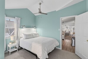 Ein Schlafzimmer mit einem Bett, Nachttischen, einem Deckenventilator und einem Fenster mit Vorhängen.