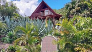 Une maison avec un toit rouge et des murs blancs, entourée d’une végétation tropicale.