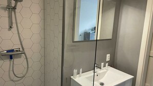 A bathroom with a glass shower enclosure, a white sink, and a mirror.