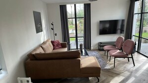 A modern living room with a sofa, chairs, a TV, and a large window.