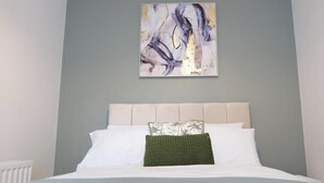 Ein Schlafzimmer mit einem Bett, Kissen, einem an der Wand hängenden abstrakten Gemälde und einer Heizung.