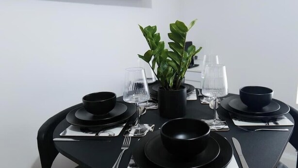 Ein Esstisch mit schwarzen Tellern, Schüsseln, Besteck und Gläsern, in der Mitte ein Blumentopf.