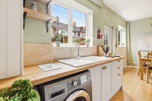 Una cocina con lavadora, un lavabo y ventana con vistas a una zona residencial.